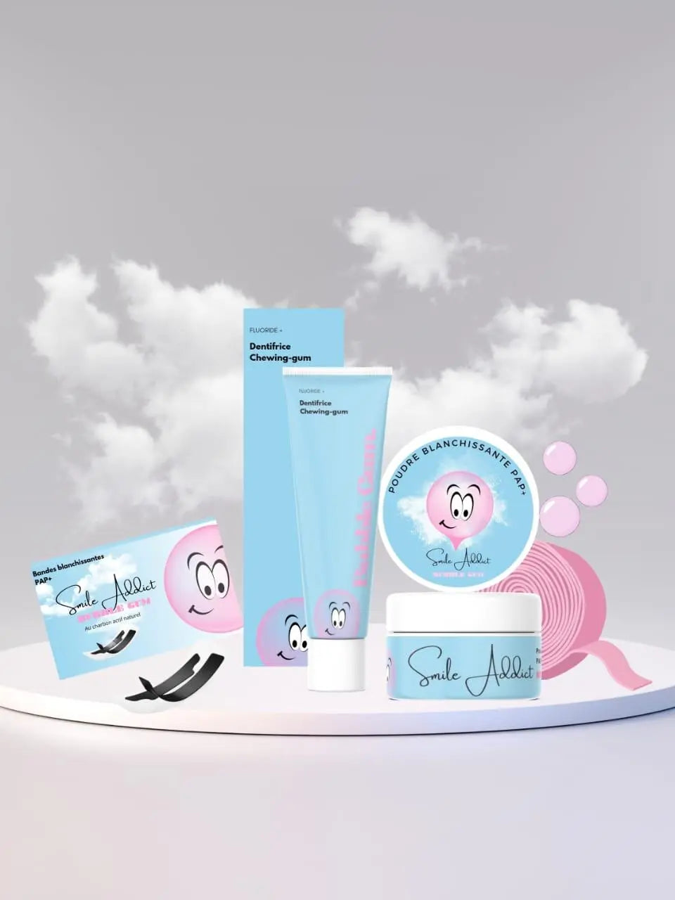 A display of Smile Addict's Pack Xtreme Blancheur Bubble Gum—Bandes PAP+, charbon, poudre, et dentifrice—features blue and pink packaging with a smiling cartoon face, set against a cloudy background.