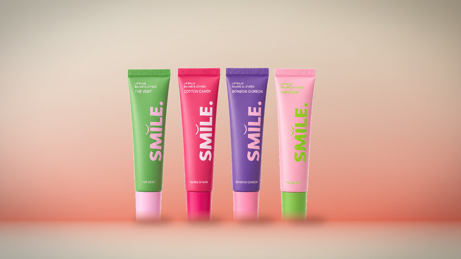 Lot de 4 Baumes à Lèvres Smile Addict, saveurs Thé Vert, Cotton Candy, Bonbon Ourson et Pastèque, fond dégradé corail