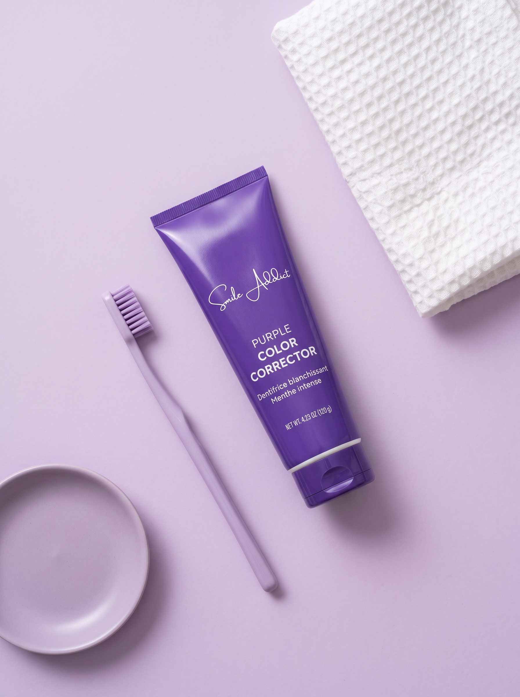 Tube de Dentifrice Violet V34 Smile Addict 120 g vu de dessus sur fond lilas, avec brosse à dents, coupelle et serviette