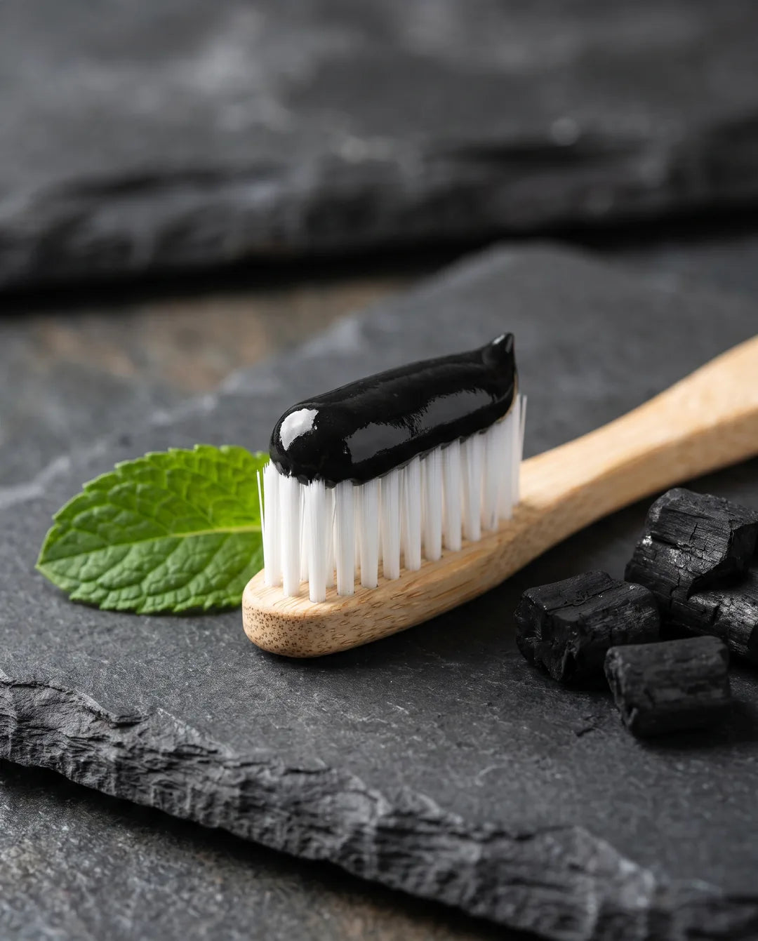 Pâte noire au charbon actif sur une brosse à dents en bambou, avec une feuille de menthe et du charbon